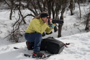 Female hotographer with long lens and snowshoes taking photos in snow in Park City.